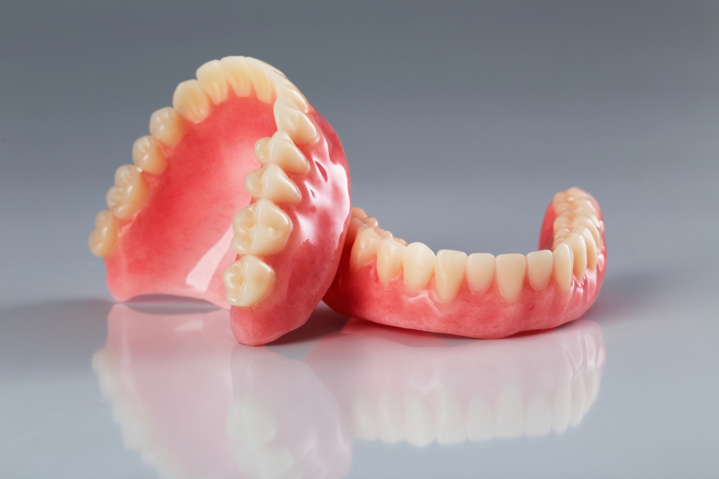 A pair of full dentures, one upper and one lower, positioned to display their pink gum-like bases and white teeth